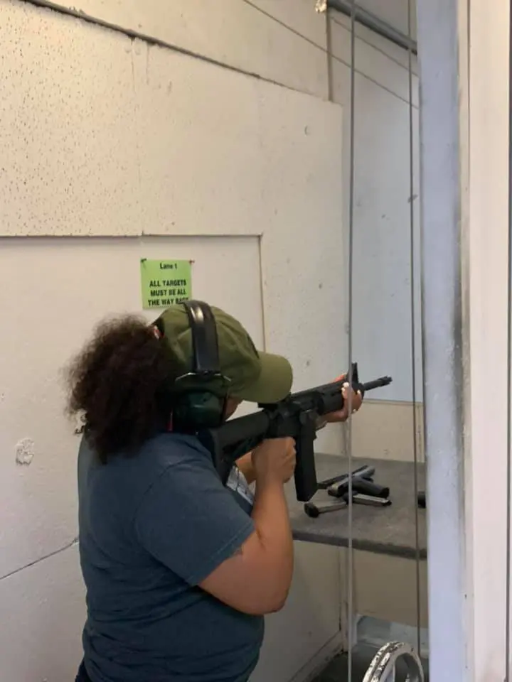 Person aiming a rifle indoors, reflected in a mirror.